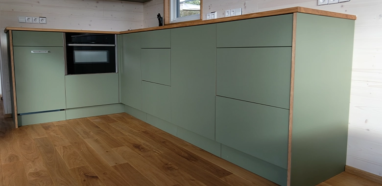 Kleinernomade-modulhouse-modell10-tinyhouse-780x380-1 Detailansicht einer Küchenzeile in einem Tiny House mit salbeigrünen Fronten und Holzarbeitsplatte.