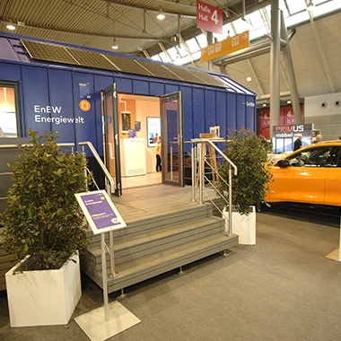 kleiner-nomade-promotion-tiny-house-enew-messe Individuelles blaues Tiny House mit Solarmodulen für eine Promotion in einer Messehalle.