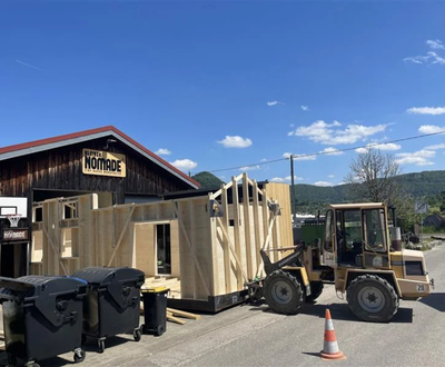 Modulares Tiny House mit Holzfassade und Metall-Dach auf einem unbebauten Grundstück.