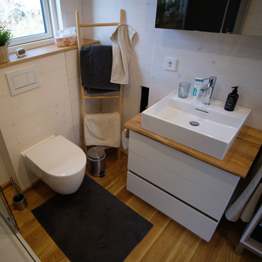 Kleines Badezimmer mit wandhängendem WC, Holzleiter als Handtuchhalter, weißem Waschbecken auf Holzarbeitsplatte und schwarzer Badematte