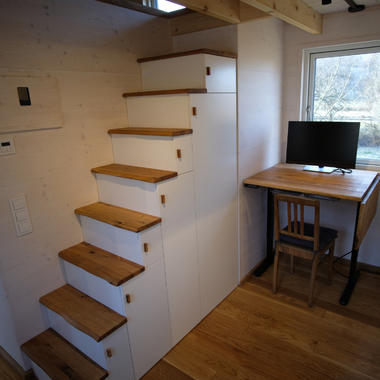 Kleine Holztreppe mit weißen Seitenwänden neben einem Holzschreibtisch mit Stuhl vor einem Fenster